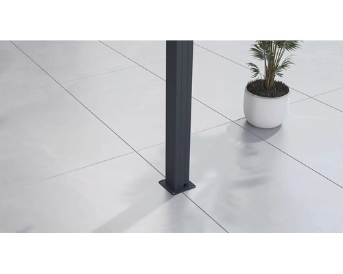 Detail antracitového sloupku s podlahovou deskou na světlé terasové dlažbě vedle rostliny v květináči.