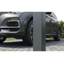 Detailní záběr na čtvercový kovový sloupek pro přístřešek pro auto na dlážděné příjezdové cestě vedle šedého auta.