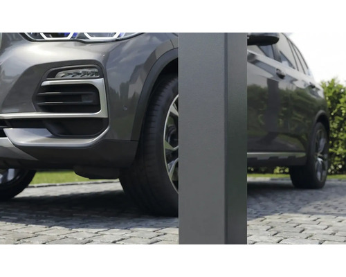 Detailní záběr na čtvercový kovový sloupek pro přístřešek pro auto na dlážděné příjezdové cestě vedle šedého auta.