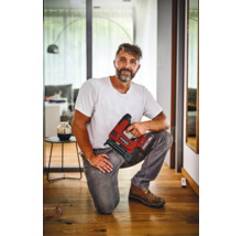 Řemeslník klečí na dřevěné podlaze a drží akumulátorovou sponkovačku Einhell v moderním interiéru.