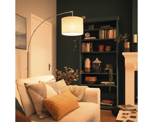 Moderní oblouková lampa s látkovým stínidlem vedle pohovky v útulném obývacím pokoji s tmavou knihovnou a krbem.