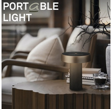 Moderní přenosná LED stolní lampa s válcovou základnou umístěná na dřevěném stole v útulném obývacím pokoji.