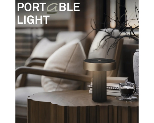 Moderní přenosná LED stolní lampa s válcovou základnou umístěná na dřevěném stole v útulném obývacím pokoji.