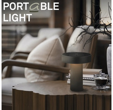 Přenosná LED stolní lampa na dřevěném stole v útulném obývacím pokoji s křesly a dekorací.