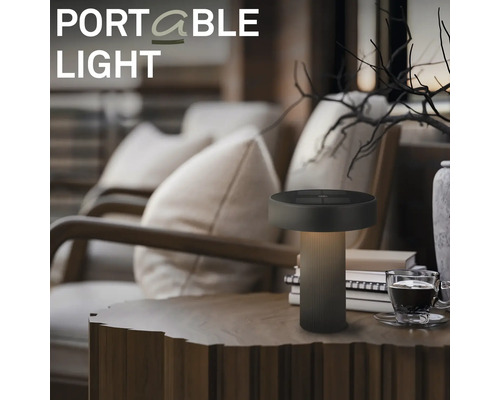Přenosná LED stolní lampa na dřevěném stole v útulném obývacím pokoji s křesly a dekorací.