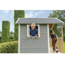 Dětský hrací domek s dítětem v okně a dívkou na verandě v zahradě