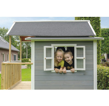 Dvě děti vykukují z okna dřevěného hracího domku.