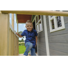 Chlapec stojí na verandě dřevěného hracího domu s okny.