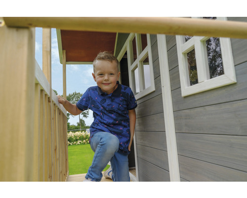 Chlapec stojí na verandě dřevěného hracího domu s okny.