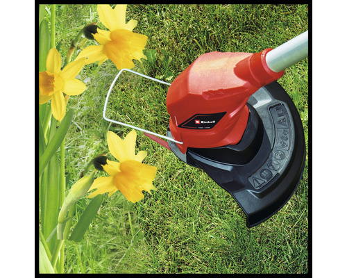 Logo Einhell. Strunová sekačka v provozu na trávníku vedle narcisů.