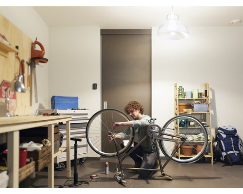 Muž opravuje kolo v dílně s pracovním stolem a regálem