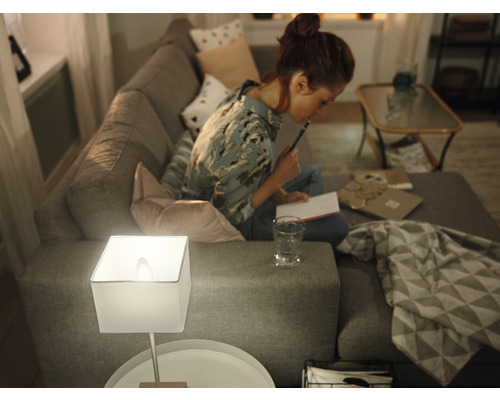 Žena sedí na pohovce se stolní lampou a zápisníkem