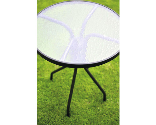 Kulatý zahradní stůl se skleněnou deskou a kovovým rámem na trávníku