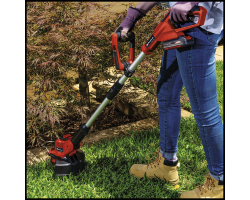 Osoba obsluhuje akumulátorový vyžínač na zahradě.