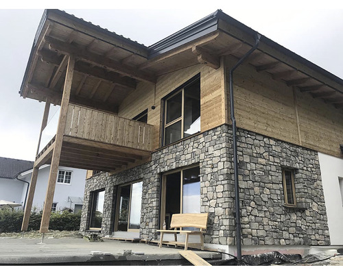 Fasáda domu s dřevěným obkladem v horním patře a kamenným obkladem v přízemí a dřevěným balkonem.