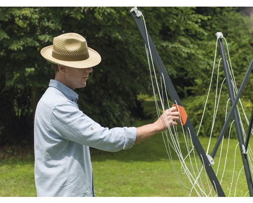 Muž rozkládá venkovní otočný sušák na prádlo.