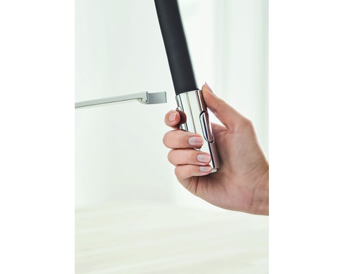 Ruka drží nastavitelnou sprchovou tyč z kovu