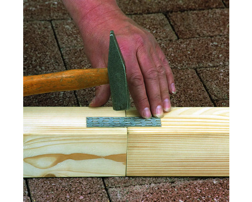 Řemeslník připevňuje děrovanou desku kladivem ke dvěma dřevěným trámům