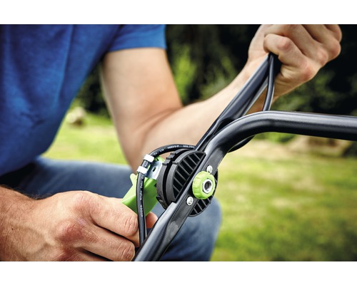 Detailní záběr osoby držící rukojeť sekačky na trávu