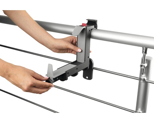 Osoba montuje držák truhlíku na balkoně na zábradlí.