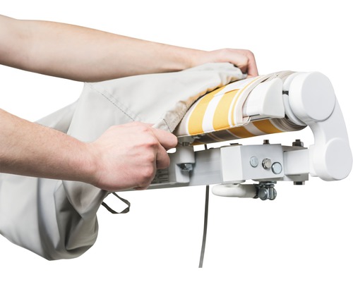 Osoba natahuje ochranný kryt na markýzu s pruhovaným vzorem.