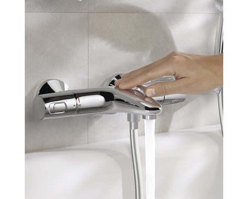 Snímek ruky ovládající chromovanou sprchovou baterii, ze které teče voda.