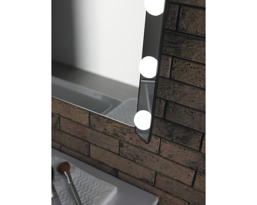 Detail osvětleného zrcadla vedle cihlové zdi v koupelně