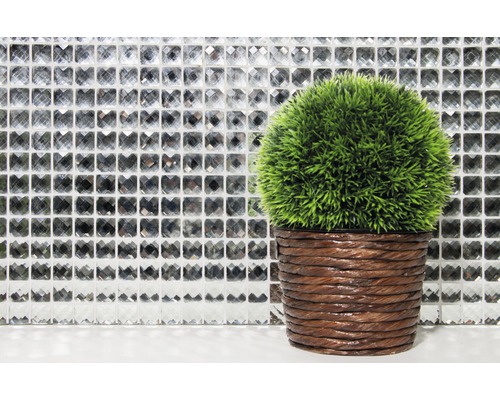 Dekorativní zelená umělá rostlina v hnědém květináči před mozaikovou stěnou