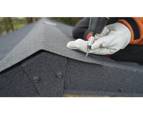 Řemeslník připevňuje střešní šindele na střechu pomocí akumulátorového šroubováku.