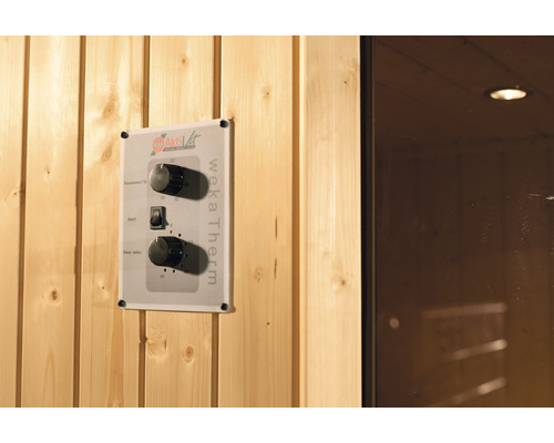 Detailní pohled na ovládání sauny Weka Therm s regulací teploty, startovacím tlačítkem a časovačem na dřevěné stěně