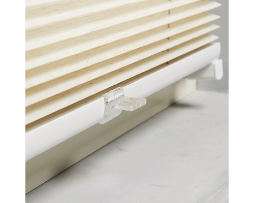 Detail béžové plisované žaluzie s bílým držákem pro dekoraci oken.