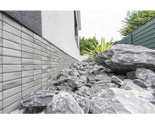 Stěna domu s obkladem soklu a kameny v zahradě