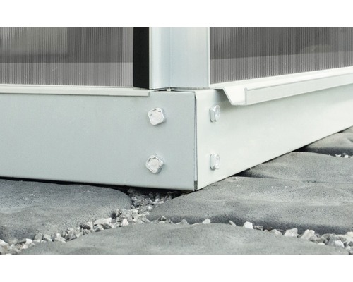 Detailní pohled na základ skleníku se šrouby na kamenné podlaze