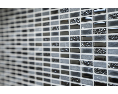 Detailní záběr stěny s mozaikovými dlaždicemi v různých odstínech šedé a texturách.