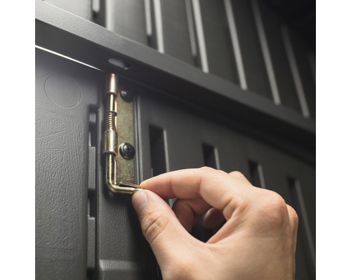 Detailní pohled na ruku upevňující kovovou západku na šedou plastovou skříň.