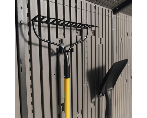 Zahradní hrábě se žlutou rukojetí a lopata, připevněné ke skladové stěně