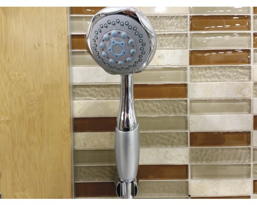 Kovová ruční sprcha na pozadí koupelny.