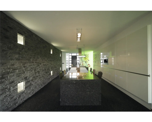 Světlá místnost s kamennou dekorativní stěnou, jídelním stolem a kuchyňskou linkou.