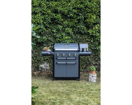 Tmavě šedý plynový gril se čtyřmi hořáky a bočními stolky na zahradě