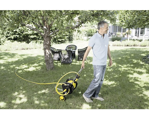 Osoba táhne vozík na zahradní hadici po trávníku