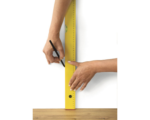 Osoba kreslí čáru tužkou a vodováhou na zeď.