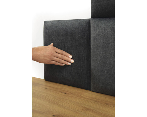 Osoba se dotýká šedého stěnového panelu s textilním potahem na dřevěné podlaze.