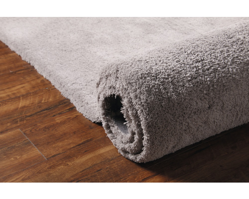Šedý koberec na dřevěné podlaze, částečně srolovaný
