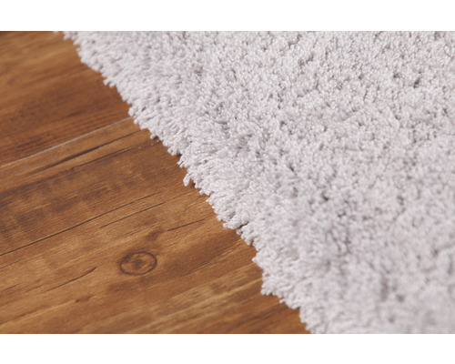 Detailní pohled na světlý koberec s vysokým vlasem na dřevěné podlaze