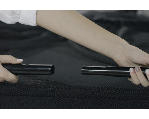 Osoba montuje trampolínu spojením dvou černých kovových tyčí.