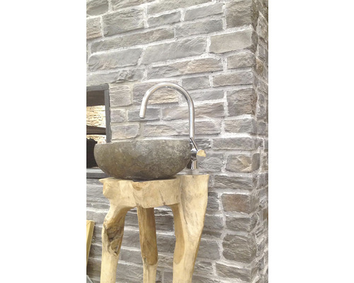 Kamenné umyvadlo na dřevěném stojanu s baterií před kamennou zdí