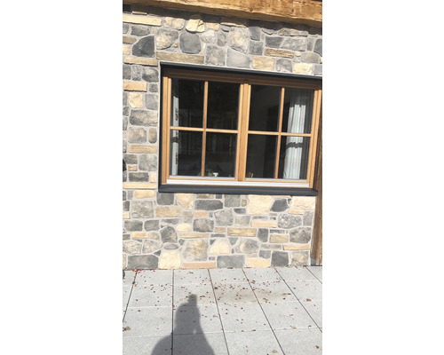 Detail okna s dřevěným rámem v domě s kamenným zdivem.