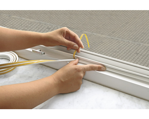 Osoba připevňuje samolepicí těsnicí pásku na okno.