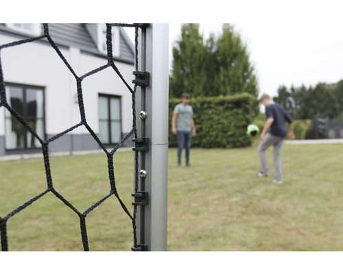 Detailní pohled na fotbalovou branku se sítí a dvěma hrajícími osobami v pozadí