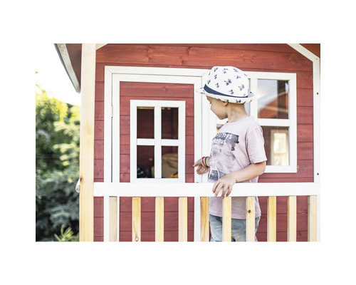 Dítě stojí před červeným dřevěným hracím domkem s bílými prvky